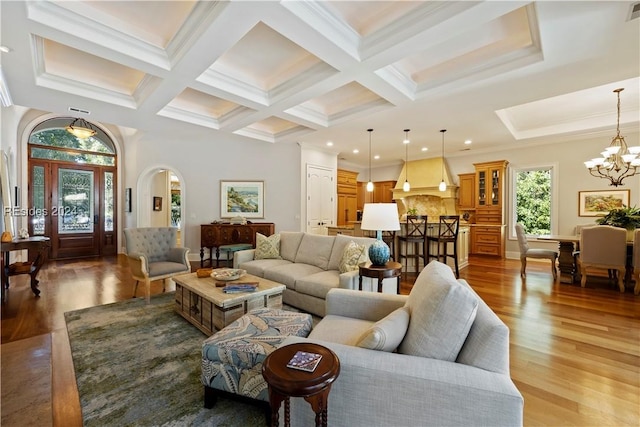 living room with coffered ceiling, wood-type flooring, ornamental molding, a notable chandelier, and beamed ceiling