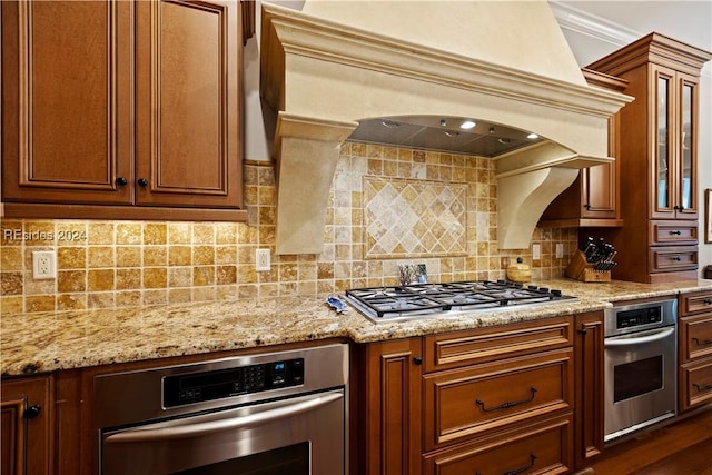 kitchen featuring backsplash, ornamental molding, stainless steel appliances, light stone countertops, and custom range hood