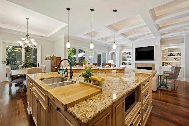 kitchen with sink, a large island with sink, coffered ceiling, light stone countertops, and beamed ceiling