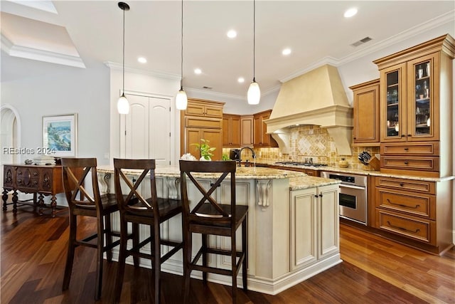 kitchen with a spacious island, a breakfast bar area, appliances with stainless steel finishes, custom range hood, and pendant lighting