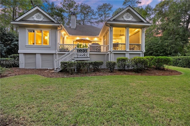 back house at dusk with a wooden deck, ceiling fan, and a lawn