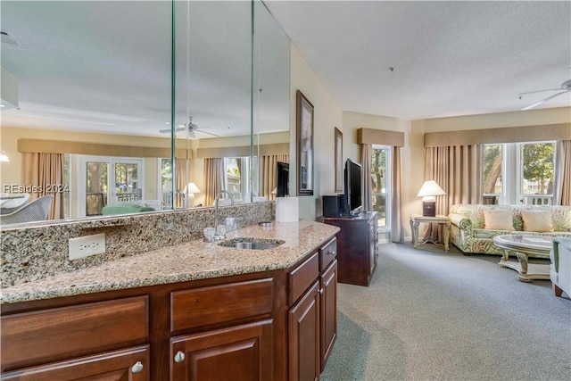 kitchen featuring sink, light stone counters, decorative light fixtures, light carpet, and ceiling fan