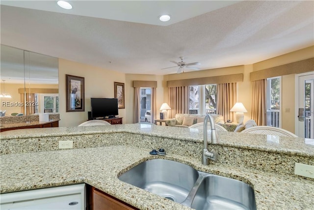 kitchen featuring ceiling fan, light stone countertops, sink, and a textured ceiling