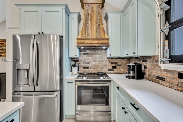 kitchen featuring premium range hood, appliances with stainless steel finishes, light stone countertops, and decorative backsplash