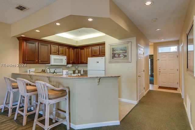 kitchen with a breakfast bar, dark colored carpet, kitchen peninsula, light stone countertops, and white appliances