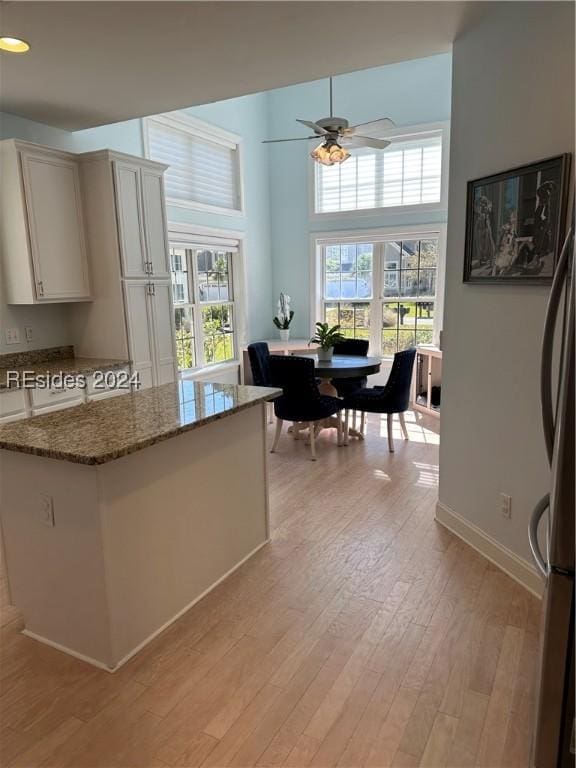 kitchen with stainless steel refrigerator, a towering ceiling, light hardwood / wood-style floors, white cabinets, and dark stone counters