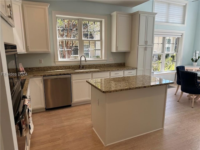 kitchen with sink, white cabinetry, stainless steel dishwasher, a kitchen island, and stone counters