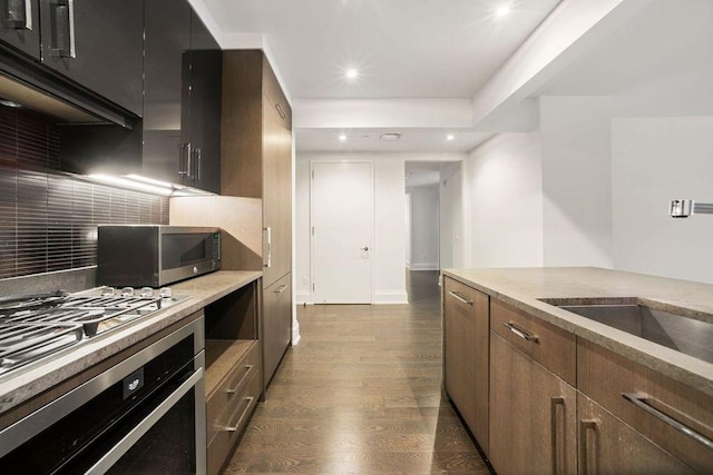 kitchen featuring dark hardwood / wood-style floors, extractor fan, stainless steel appliances, light stone countertops, and tasteful backsplash