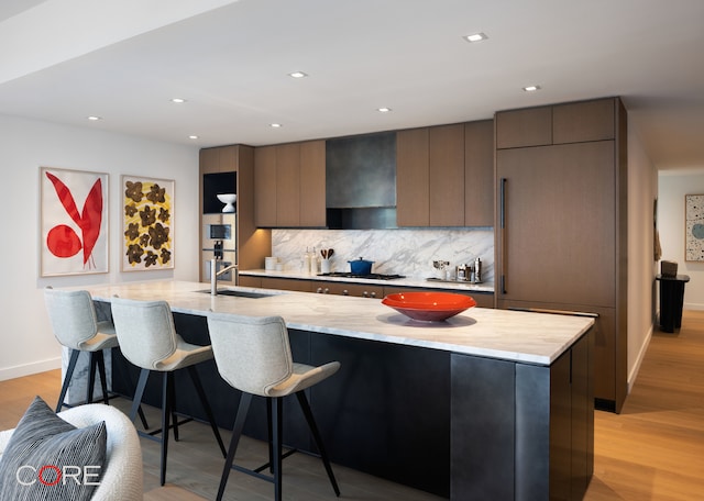 kitchen featuring tasteful backsplash, stainless steel gas stovetop, light hardwood / wood-style flooring, wall chimney exhaust hood, and sink