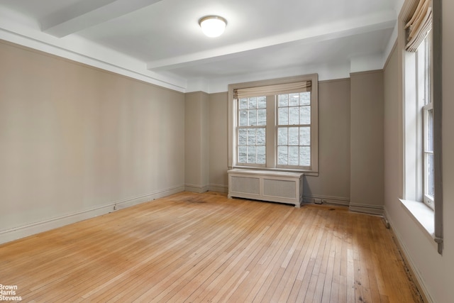 empty room featuring radiator heating unit, light hardwood / wood-style flooring, and beamed ceiling