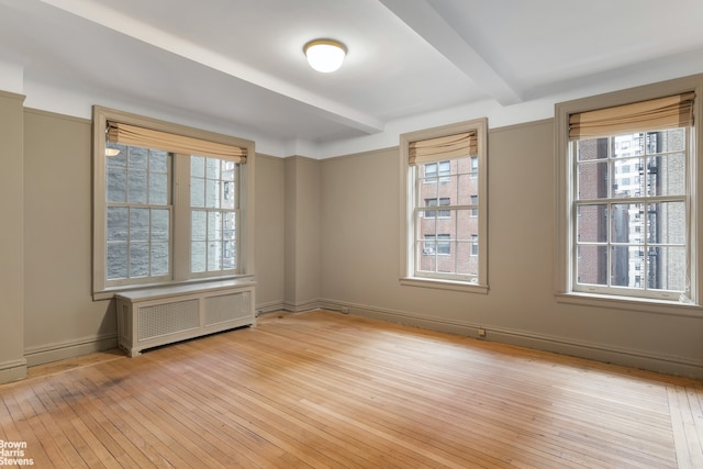 empty room featuring beam ceiling, radiator, and light wood-type flooring