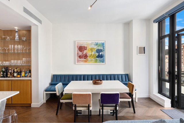 dining space with dark parquet flooring and bar