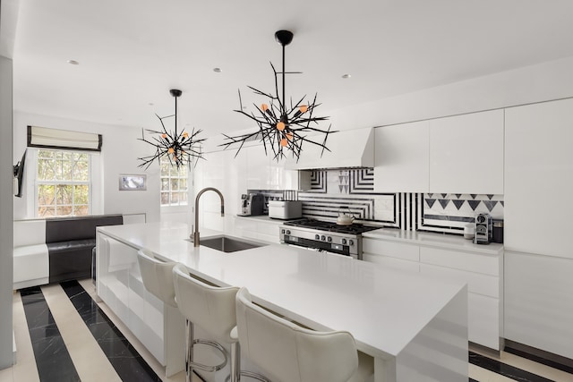 kitchen featuring backsplash, decorative light fixtures, white cabinetry, and a center island with sink