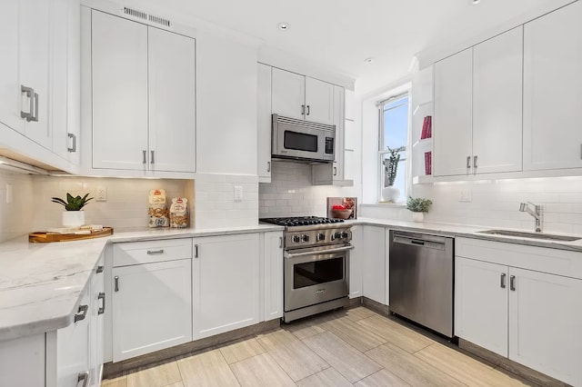 kitchen featuring tasteful backsplash, appliances with stainless steel finishes, light stone countertops, white cabinetry, and sink