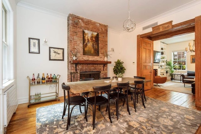 dining space with a chandelier, light hardwood / wood-style floors, brick wall, a brick fireplace, and crown molding