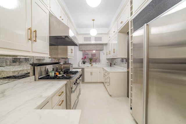 kitchen with white cabinets, backsplash, high end appliances, light stone counters, and pendant lighting