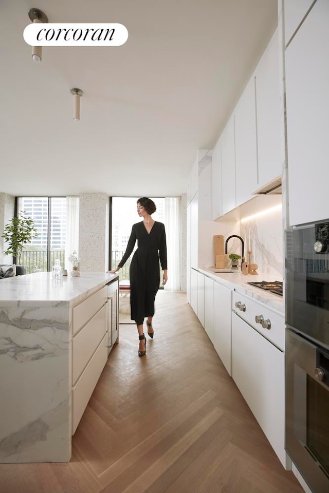 kitchen with light parquet floors, light stone countertops, sink, and white cabinets