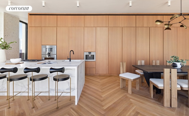 kitchen with light parquet floors, pendant lighting, a breakfast bar, stainless steel appliances, and light stone counters