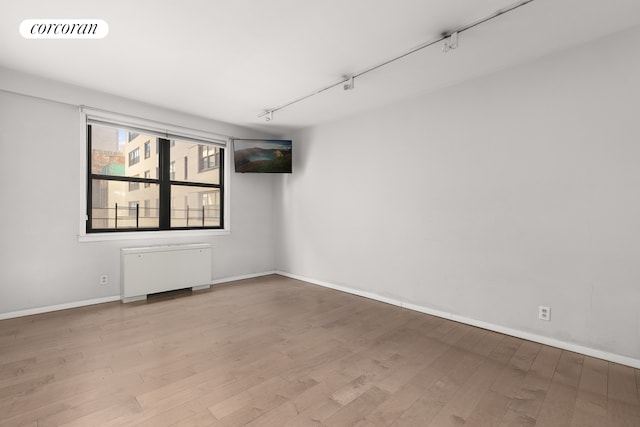 empty room with rail lighting, radiator, and hardwood / wood-style floors