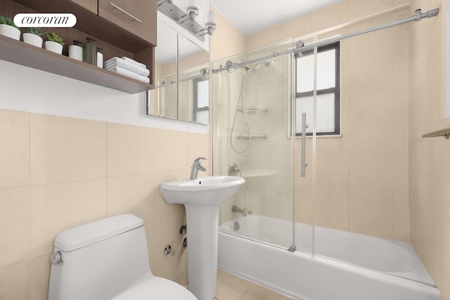 bathroom featuring tile walls, toilet, and bath / shower combo with glass door