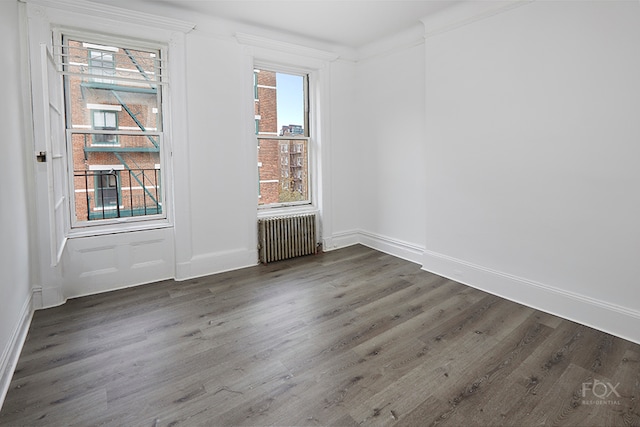 unfurnished room featuring a healthy amount of sunlight, radiator, dark hardwood / wood-style floors, and ornamental molding