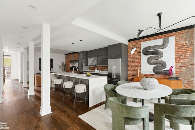 dining room featuring sink, decorative columns, brick wall, and dark hardwood / wood-style floors