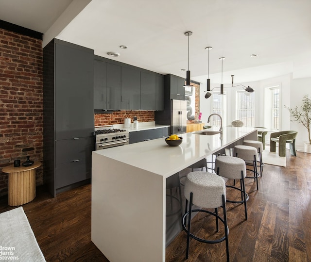 kitchen with high quality appliances, an island with sink, a kitchen bar, dark hardwood / wood-style floors, and hanging light fixtures