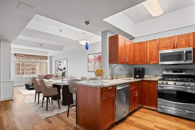 kitchen featuring pendant lighting, light stone countertops, light wood-type flooring, kitchen peninsula, and appliances with stainless steel finishes