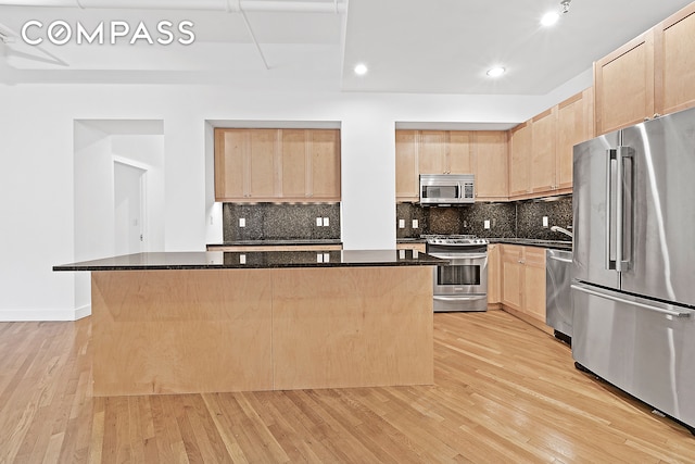 kitchen featuring appliances with stainless steel finishes, a kitchen island, tasteful backsplash, dark stone counters, and light wood-type flooring