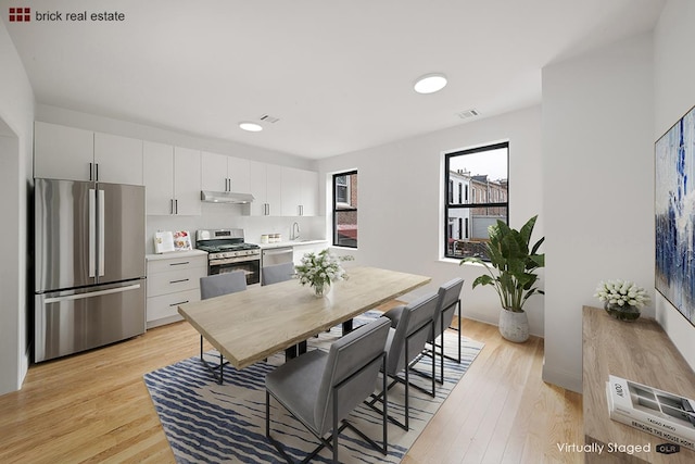 kitchen featuring stainless steel appliances, light hardwood / wood-style floors, backsplash, and white cabinetry