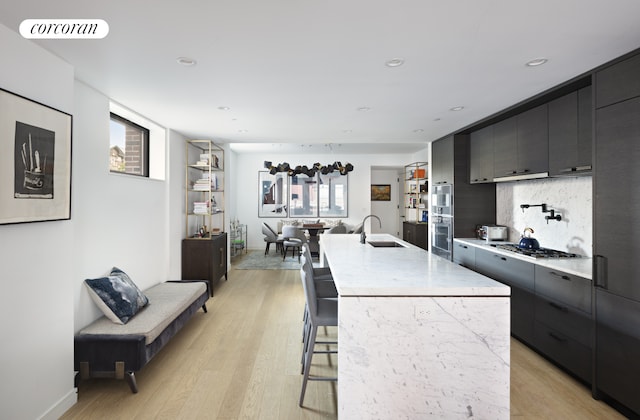 kitchen with light hardwood / wood-style flooring, a healthy amount of sunlight, a kitchen breakfast bar, and a kitchen island with sink