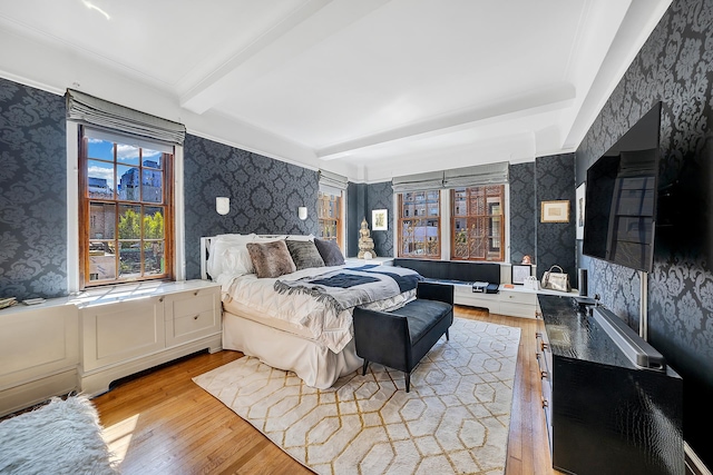 bedroom with light wood-type flooring, beamed ceiling, and multiple windows