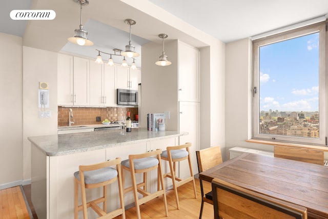 kitchen featuring white cabinetry, decorative backsplash, sink, light stone counters, and light hardwood / wood-style floors