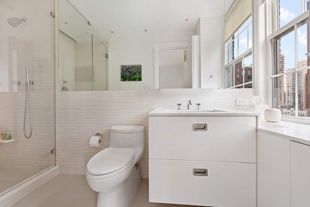 bathroom featuring tasteful backsplash, toilet, vanity, a shower with shower door, and tile walls