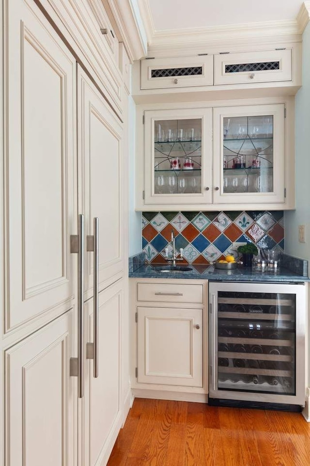 bar with tasteful backsplash, light hardwood / wood-style floors, white cabinetry, and beverage cooler