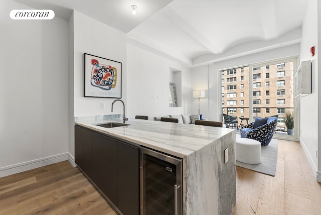 kitchen featuring beverage cooler, light hardwood / wood-style floors, light stone counters, and sink