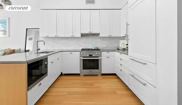 kitchen featuring black microwave, high end stainless steel range oven, sink, kitchen peninsula, and light hardwood / wood-style floors