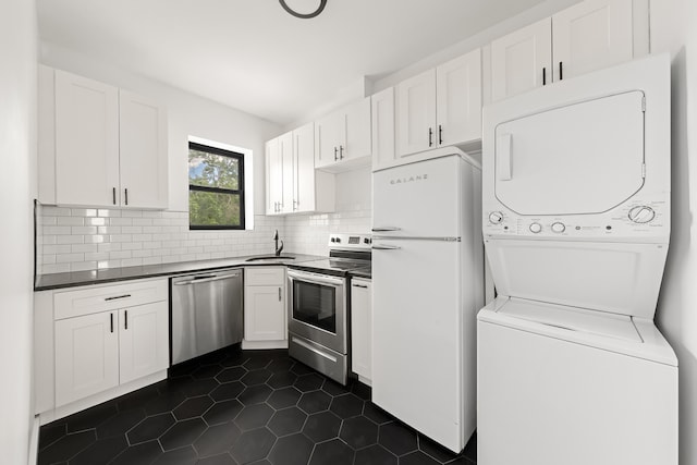 kitchen featuring stacked washer / drying machine, white cabinetry, stainless steel appliances, and dark tile patterned flooring