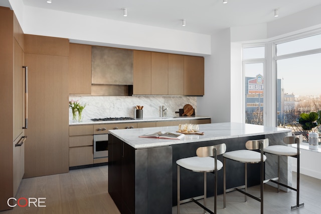 kitchen with decorative backsplash, light stone counters, light wood-type flooring, stainless steel appliances, and a kitchen island