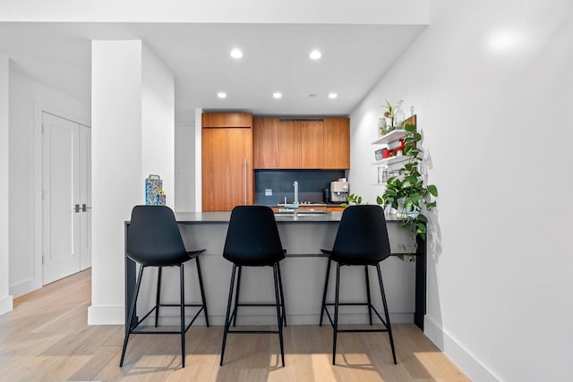 kitchen featuring light wood-type flooring, a kitchen bar, sink, and tasteful backsplash