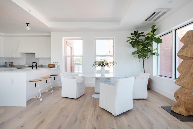 dining area with light hardwood / wood-style floors and a tray ceiling