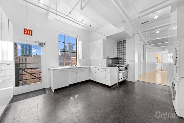 kitchen featuring white cabinetry, high end stove, backsplash, white dishwasher, and stacked washer / drying machine