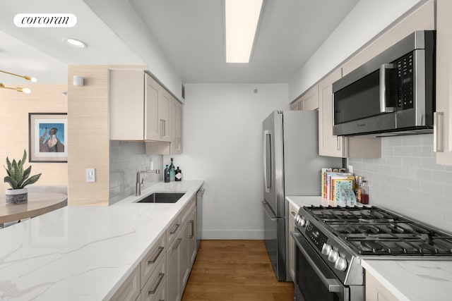 kitchen featuring backsplash, sink, light stone countertops, appliances with stainless steel finishes, and wood-type flooring