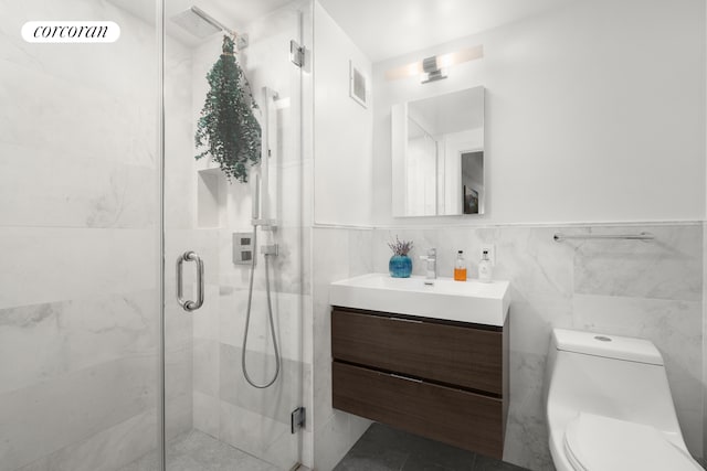 bathroom with vanity, a shower with shower door, tile walls, and toilet