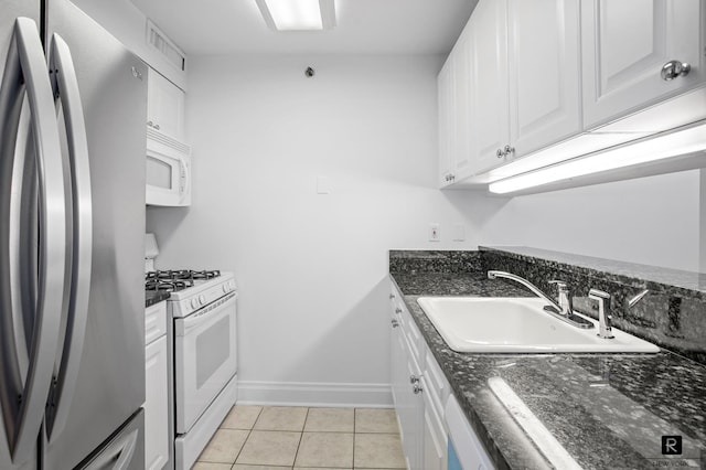 kitchen with white appliances, dark stone counters, white cabinets, sink, and light tile patterned flooring