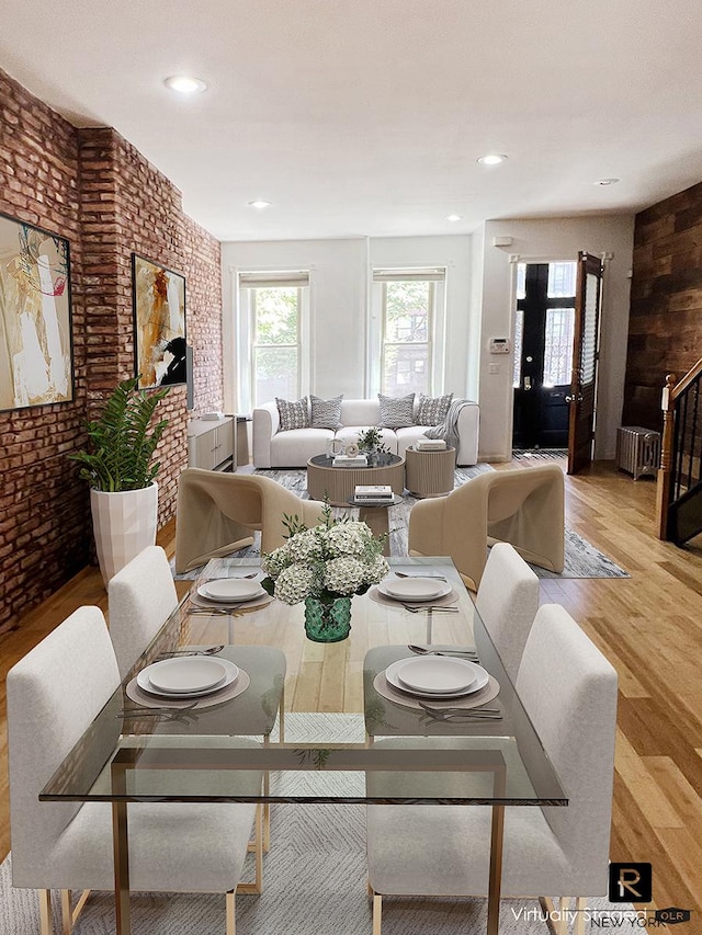 dining space featuring light wood-type flooring, radiator heating unit, and brick wall