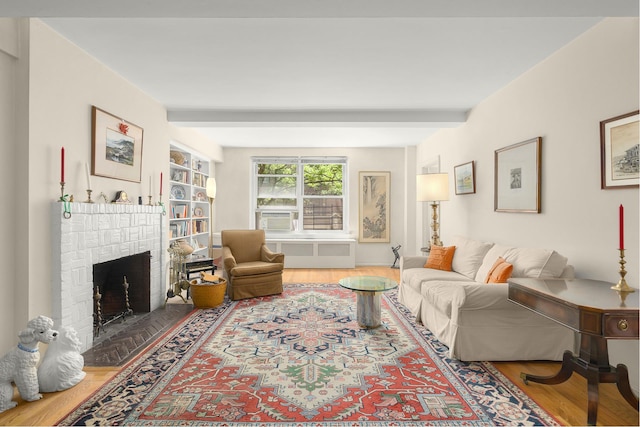 living room featuring radiator heating unit, beamed ceiling, a brick fireplace, wood-type flooring, and cooling unit