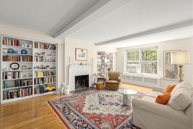 living room featuring radiator heating unit, a fireplace, beam ceiling, and light wood-type flooring