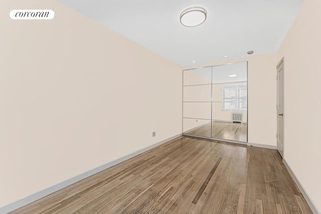 unfurnished bedroom featuring wood-type flooring, a closet, and radiator heating unit