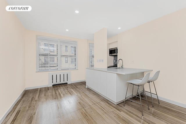 kitchen with light hardwood / wood-style flooring, white cabinets, kitchen peninsula, sink, and a kitchen bar